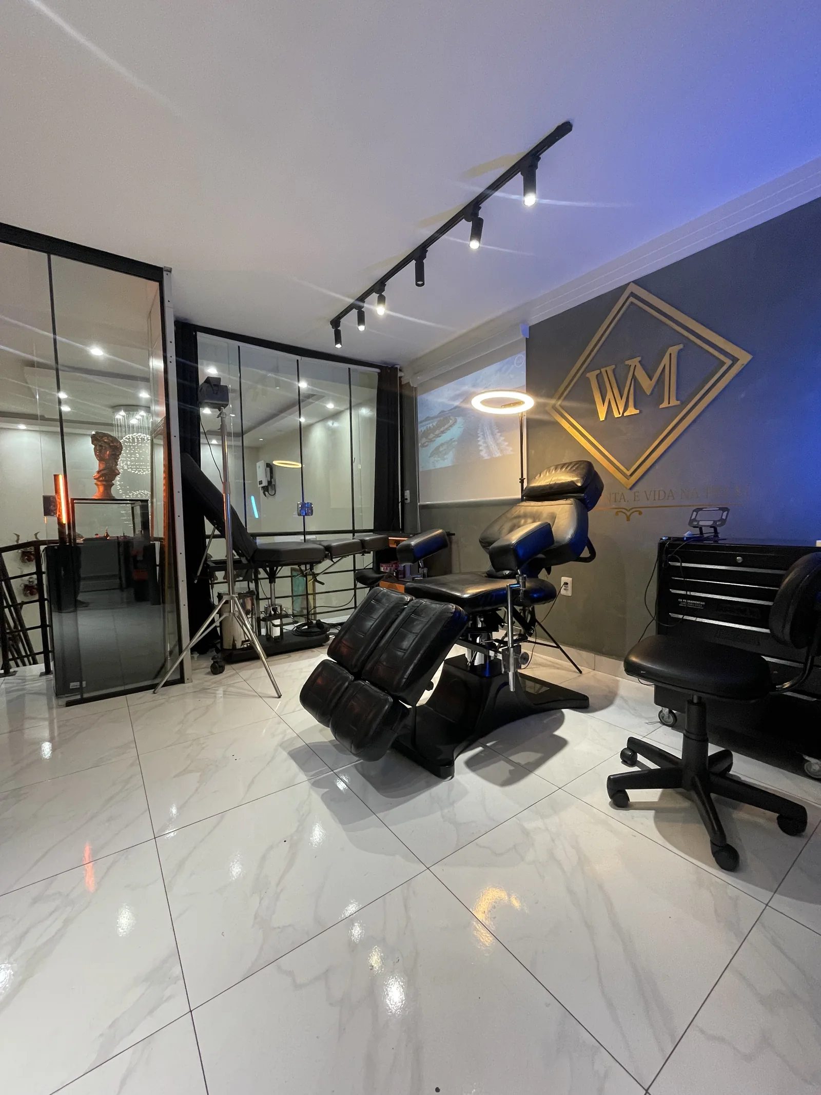 Sala de atendimento do WM Tattoo Studio, com cadeira profissional, logo dourado WM e iluminação em trilho