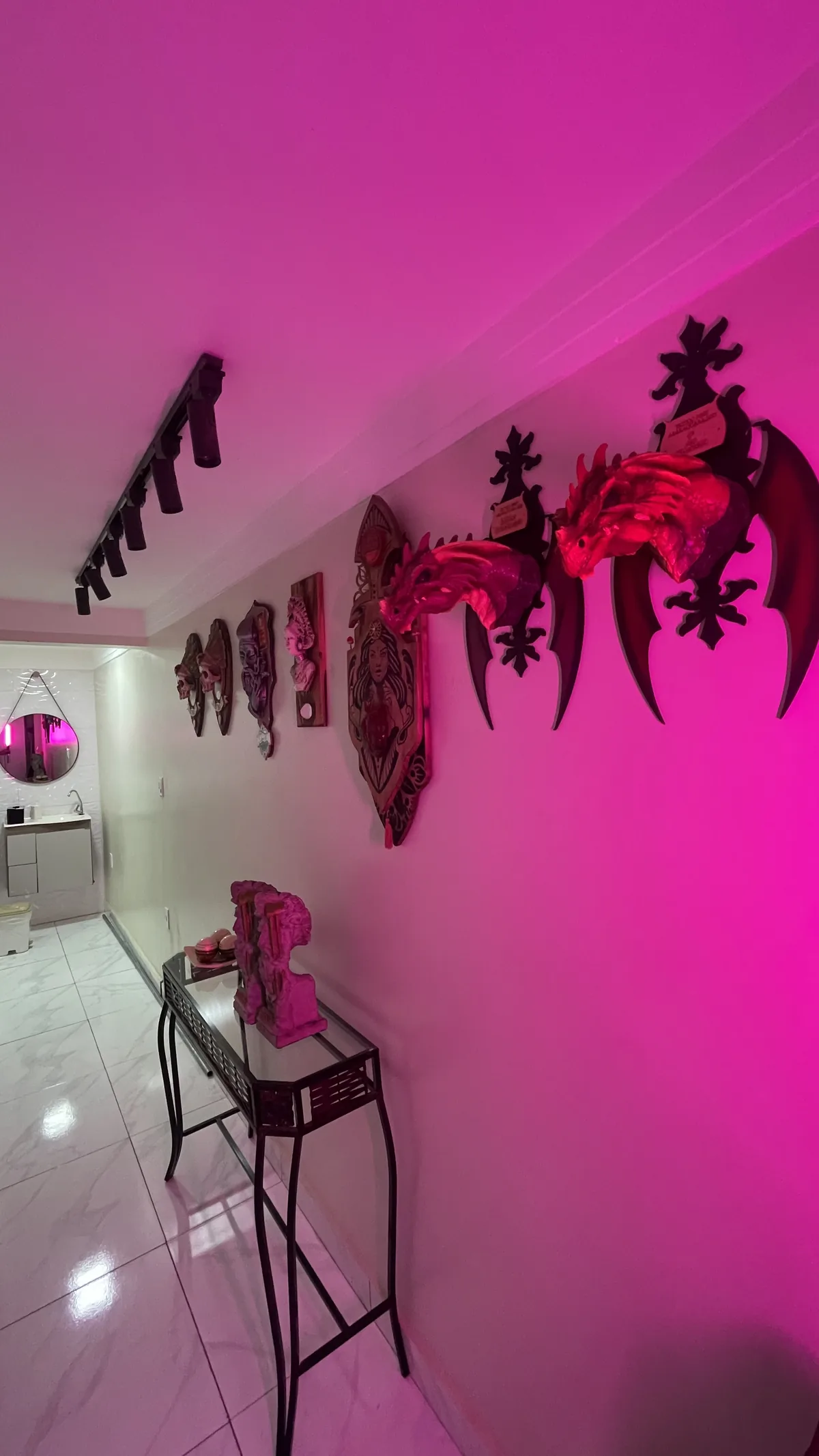 Corredor com iluminação rosa, esculturas na parede e aparador de vidro