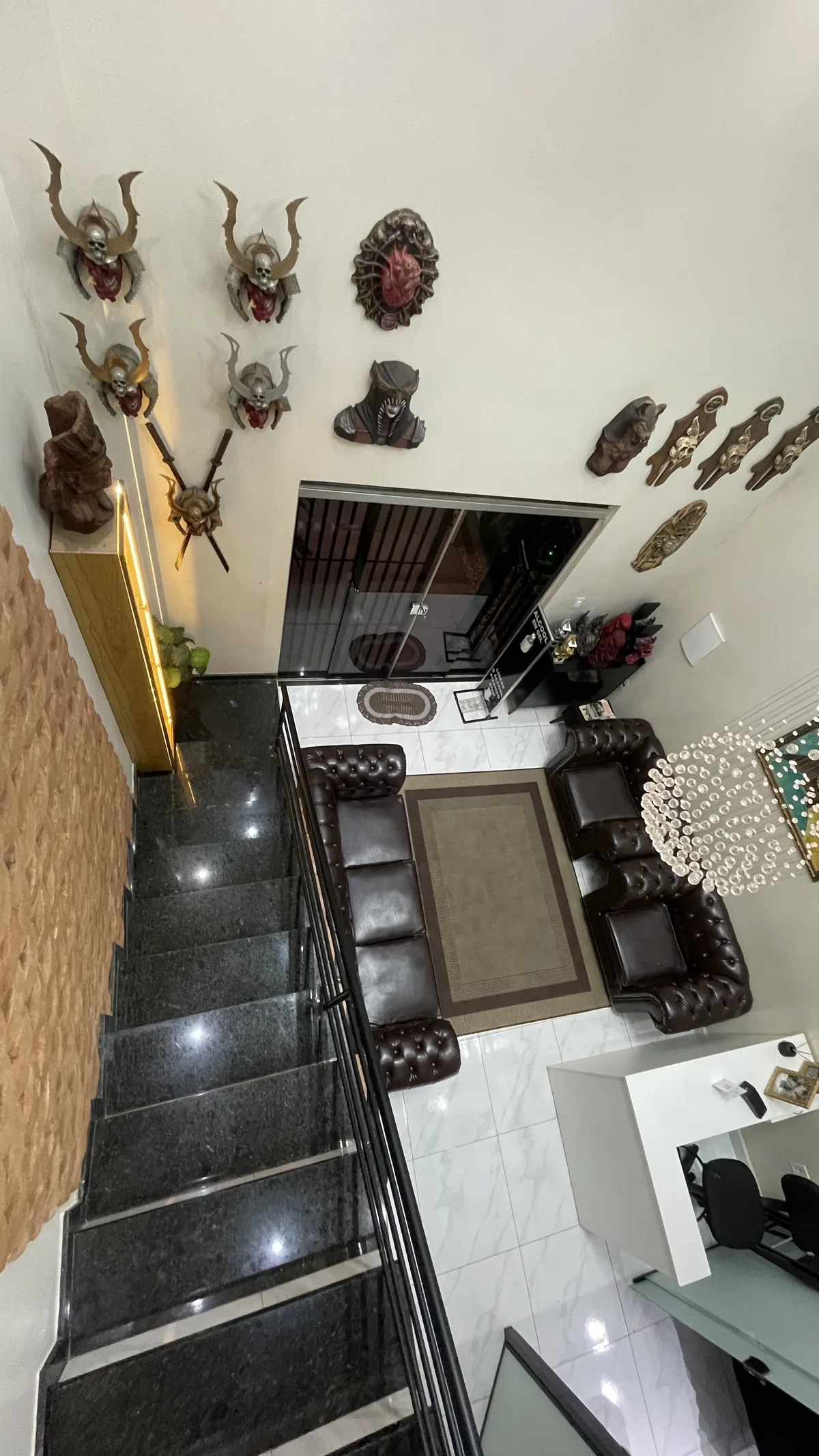 Vista do mezanino para a recepção, com escada de mármore, sofás chesterfield e máscaras na parede