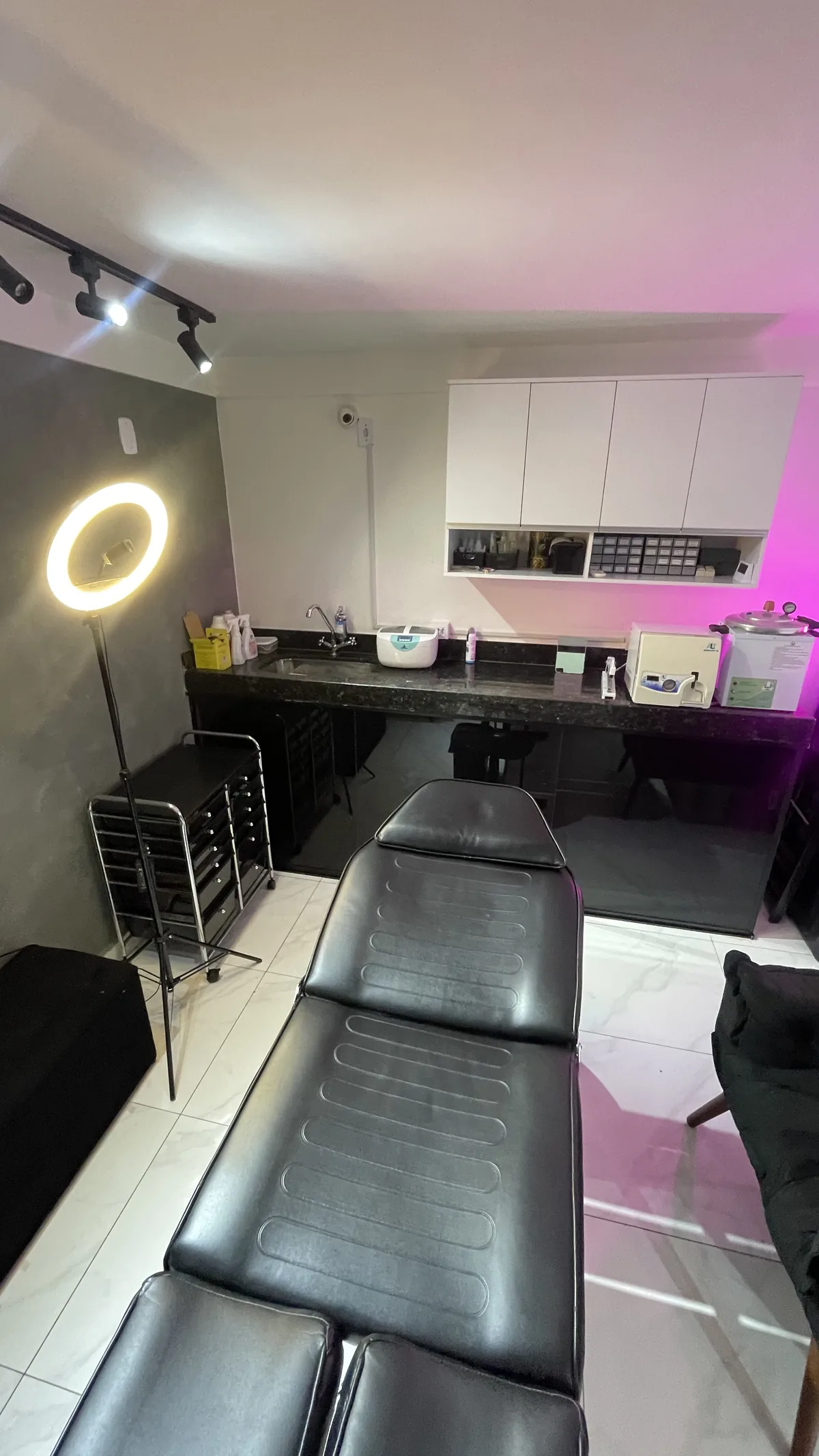 Sala de atendimento com maca preta, ring light e bancada de biossegurança